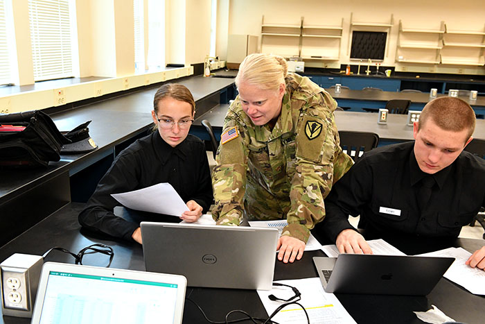 A professor helps two cadets on a computer during class