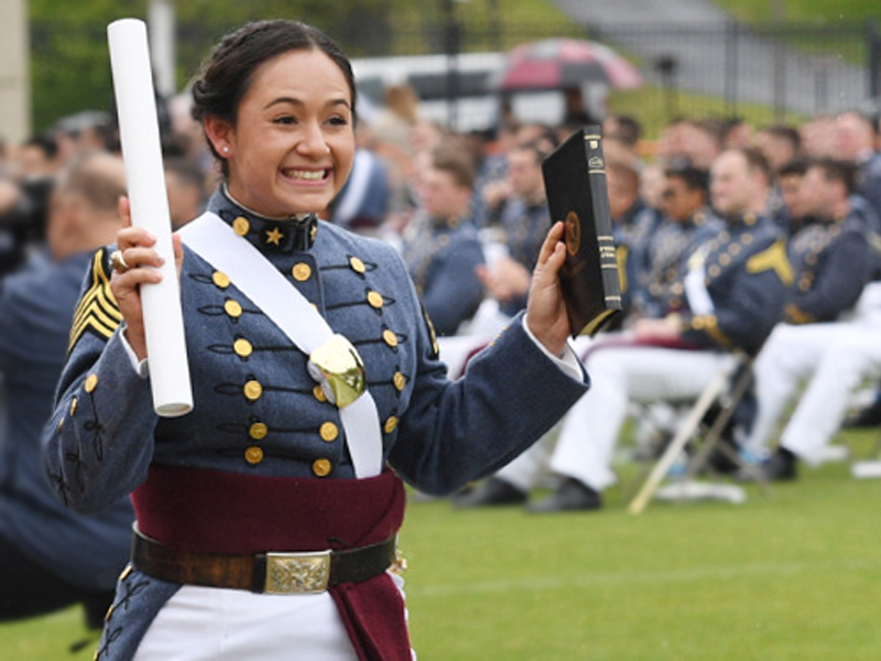 VMI cadet holding diploma and smiling during graduation as she walks back to her seat