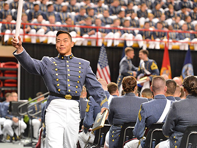A cadet waves his diploma in the air as he crosses the stage.