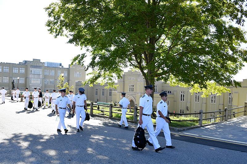 Cadets in their white summer uniforms walk under a tree on their way to class.